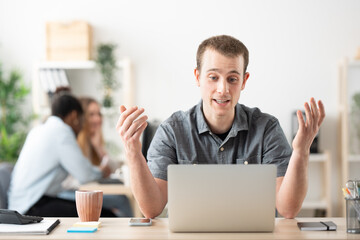 Young man having video call on laptop in the office. Freelancer talking in online meeting.