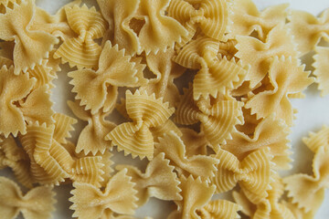 scattered raw farfalle pasta on a white marble table close-up. farfalle pasta on white background top view. butterfly pasta	