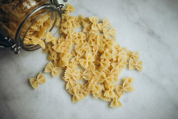 pour raw farfalle pasta from a jar onto a white marble table. scattered farfalle pasta on the table top view. butterfly pasta