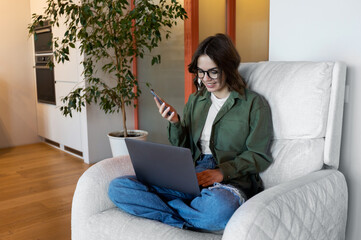 woman using laptop with phone at home