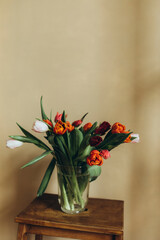 a bouquet of red and pink tulips in a transparent vase near the sand wall. bouquet of tulips in a vase on a wooden stand