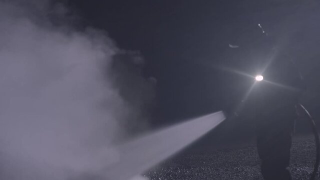 Unrecognizable fireman silhouette combating a fire of a burning car accident at night in the dark. Firefighter fighting flames with water hose. Filmed with RED camera. High quality 4k footage