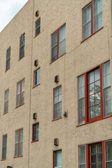 Building exterior with orange or beige stucco cement facade and red accent paint around window frames with visible glass