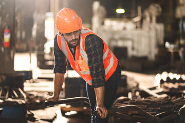 Young Asian male worker wearing safety vest jacket and hard helmet with protective glasses working in coal mine factory and warehouse using spade to move pieces of coal