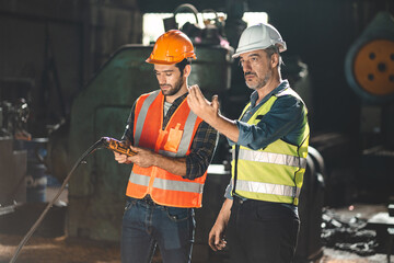 Senior male engineer training and explaining work to new employee wearing vest and safety jacket...