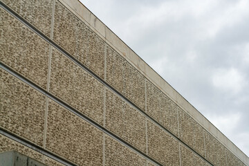 Ridged and textured building wall facade with geometric block and rectangle design with flat roof and background clouds