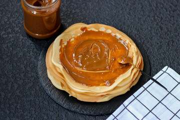 Aromatic crepes with condensed milk are lying on black shale dish, super tasty, let's try it! Top view. Print for kitchen