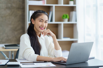 Happy young asian businesswoman sitting with laptop in office.