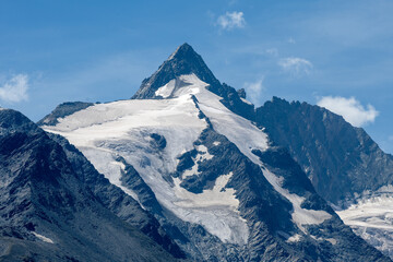Fototapeta na wymiar Mountain peak with a melting glacier on brown and grey rocks in an alpine area