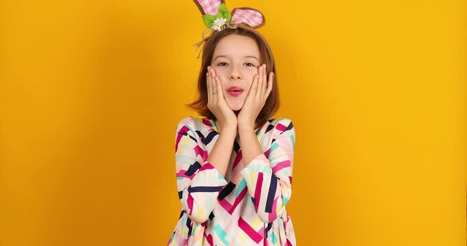 Happy playful teenager girl wearing bunny ears on a bright yellow studio background, celebrating Easter in style.