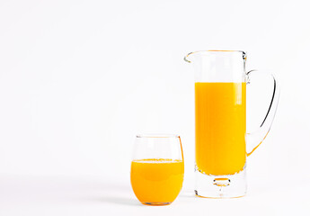 Glass carafe and glass filled with orange juice on a white background with free space 
