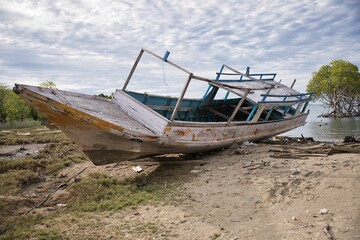 Shot of an old abandoned ship lying on the beach, in the background the sea and mangroves.