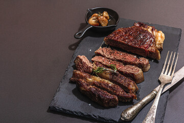 Well done roasting Ribeye steak with caramelized garlic and vintage cutlery. Hard light, dark shadow