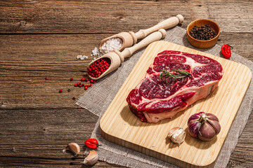 Raw Ribeye steak with spices and herbs. Dry aged meat, traditional food, hard light, dark shadow