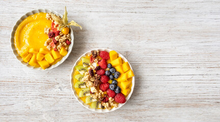 Obraz na płótnie Canvas Ywo Healthy mango smoothie bowls with blueberries, raspberries, kiwi and granola. Above view scene on a light grey wooden background.