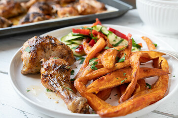 Grilled chicken with sweet potato fries and mediterranean salad on a plate