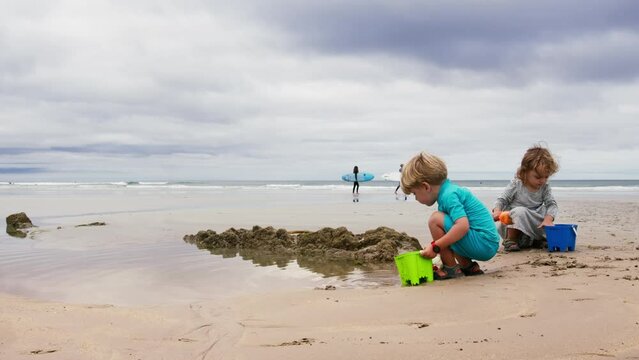 Kids play with sand on the ocean beach over surfers pass by