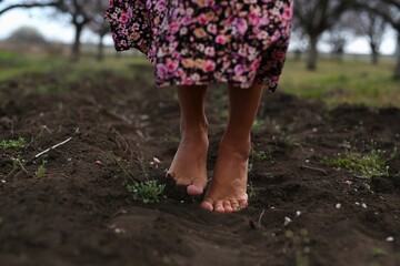 a girl with bare feet walks on fresh black earth in an apple orchard, focus on female feet, spring mood