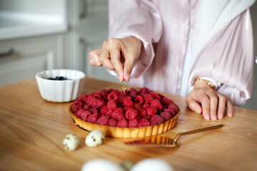 Close-up of woman's hands decorating raspberry tart, cooking delicious cake with fresh berries