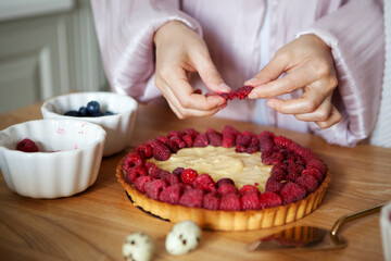 Close up of woman's hands decorating raspberry tart, cooks delicious pie with fresh berries and...