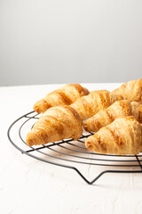 Top view of small croissants on rack on white table, selective focus, vertical, with copy space