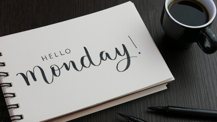 HELLO MONDAY! black lettering in notebook with cup of espresso and pens on black wooden desk - obrazy, fototapety, plakaty