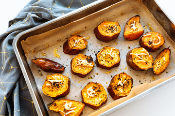 Baked sweet potato slices with herbs and olive oil on craft paper for baking in baking sheet. 