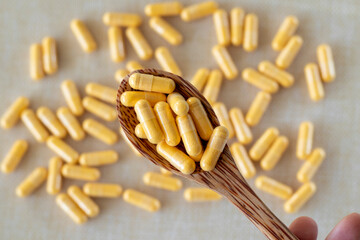 Lots of light yellow capsules in a wooden spoon on a white background. Supplements, vitamins,...