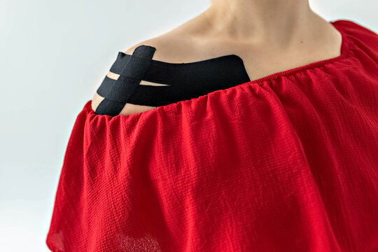 A young blonde girl in a bright red dress with a teip on her shoulder after an injury. Fixation of muscles and ligaments on the girl's shoulder with black kinesiology tape. Taping in sports