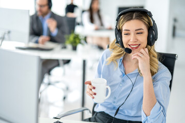 Charismatic blond hair woman agent wearing headset and holding coffee cup listening and answering...