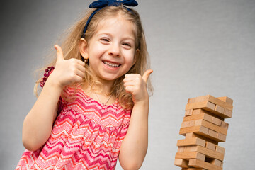 a little happy girl is playing the board game at the table. Construction of a tower made of wooden...