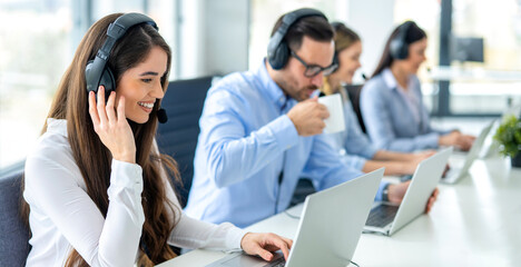 Panoramic view of beautiful young woman, customer service representative, working in call center with her colleagues using laptops.