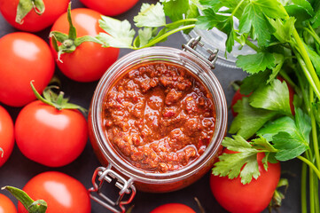 Homemade tomato sauce for pizza or pasta in a jar on a gray background with fresh vegetables and herbs close up.