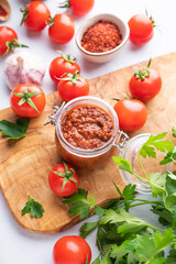 Homemade tomato sauce for pizza or pasta in a jar on a wooden board on a light background with fresh vegetables and herbs close up.