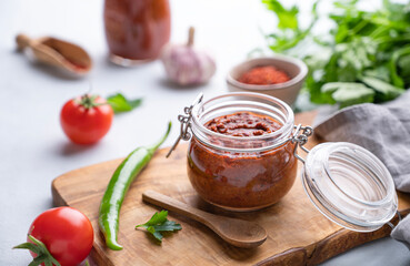 Homemade tomato sauce for pizza or pasta in a jar on a light background with fresh vegetables and herbs close up.