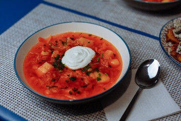 Red borscht with sour cream and horseradish on a blue tablecloth background
