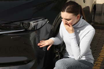 Stressed woman near car with scratch outdoors