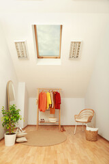 Stylish clothes rack, mirror and wicker chair in attic room. Interior design