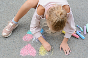 Obraz na płótnie Canvas Little child drawing butterfly and hearts with chalk on asphalt