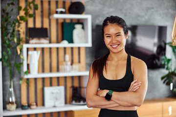 Fototapeta na wymiar Portrait of a smiling Asian fitness woman standing at home with arms crossed.