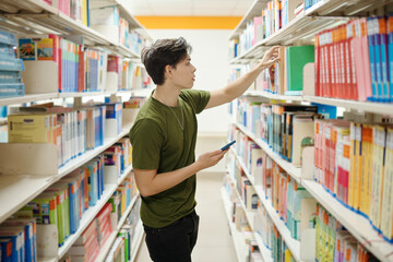 Plakat College student with smartphone taking book from shelf