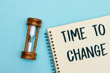Time to change concept on notebook with hourglass on wood table as time passing concept. Life time...