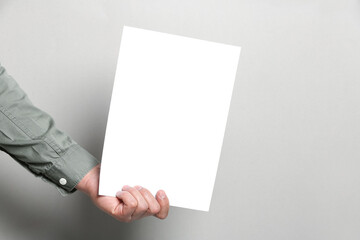 Man holding sheet of paper on grey background, closeup. Mockup for design