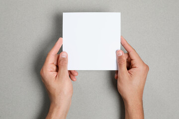 Man holding sheet of paper on grey background, closeup. Mockup for design