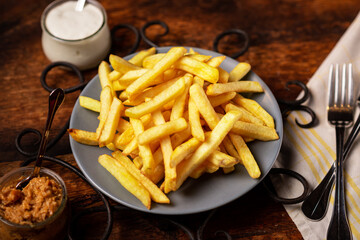 French fries on a plate on a wooden background. Golden-colored potato wedges.