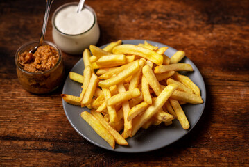 French fries on a plate on a wooden background. Mayonnaise and sauce stand side by side. Vegetarian food.