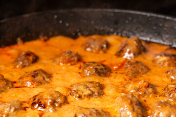 Cooking homemade meatballs in a frying pan in a sauce of tomatoes and sour cream. Close-up macro. Food background.