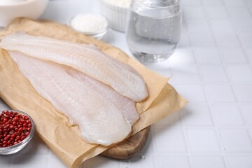 Different ingredients for soda water batter and raw fish fillet on white tiled table. Space for text