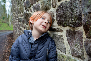 Smiling contented boy near the stone wall. A boy of nine and ten years of age with long red hair....