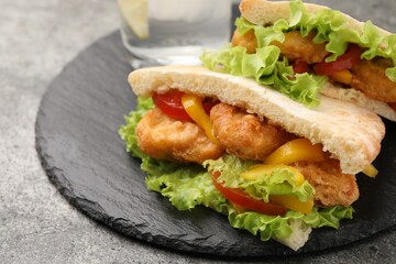 Delicious pita sandwiches with fried fish, pepper, tomatoes and lettuce on dark grey table, closeup